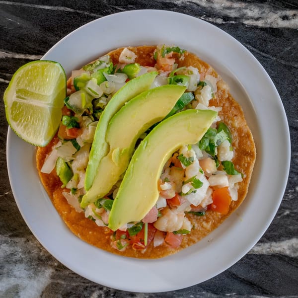 Mangonadas Mexican Kitchen's tostada with shrimp ceviche, avocado slices, and a lime wedge.