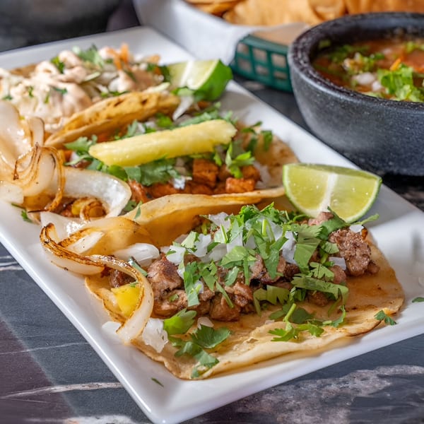 A white platter of various Mangonadas Mexican Kitchen tacos, including carne asada, al pastor, and chicken.